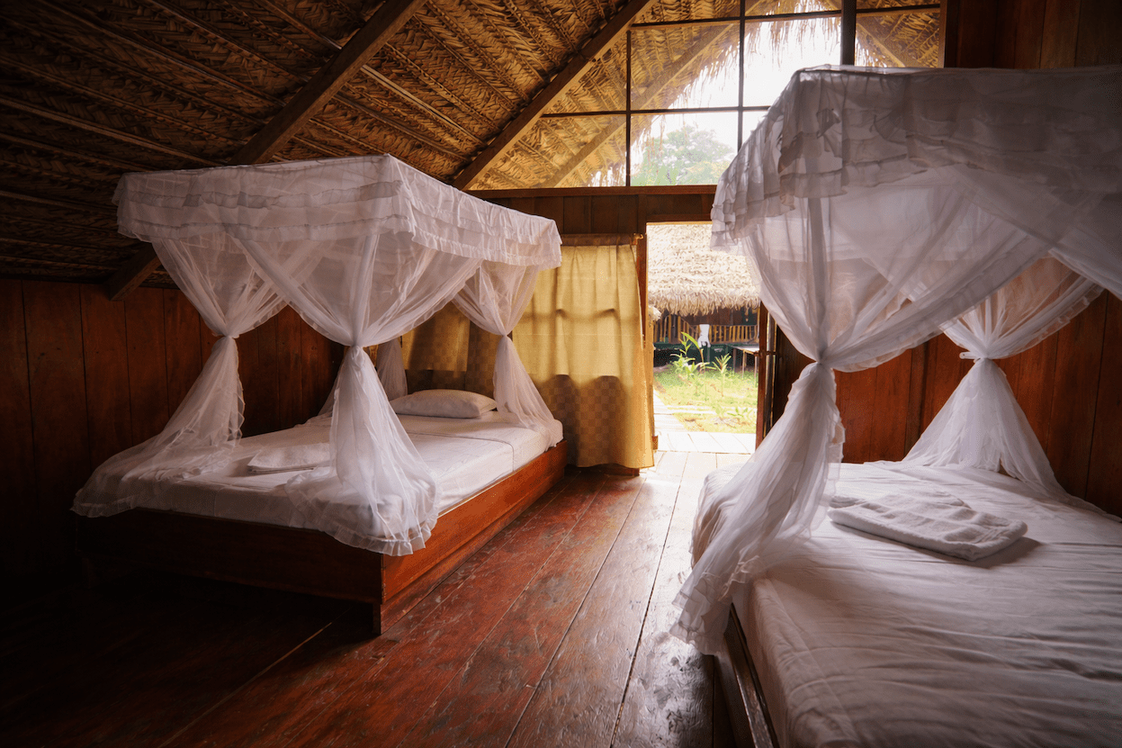 Bedroom with a mosquito-net canopy bed inside an Amazon rainforest eco-lodge cabin.