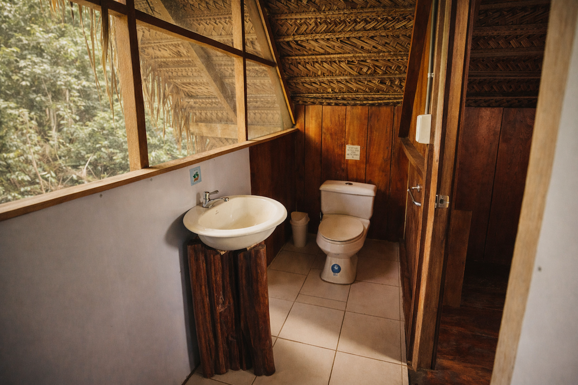 Simple private bathroom with toilet and sink inside a traditional Amazon eco-lodge cabin.