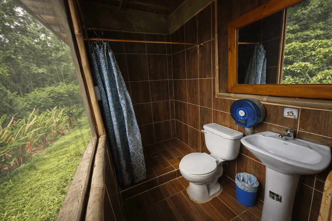 Private bathroom with shower, toilet, and sink overlooking the Amazon rainforest at an eco-lodge.