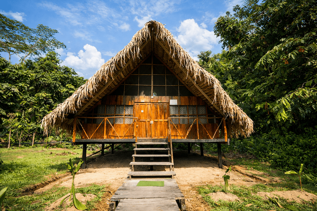 Cabaña tradicional con techo de paja en un eco-lodge de la selva amazónica, elevada y rodeada de jungla.