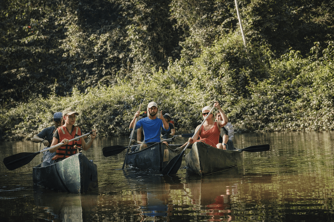 Grupo pequeño remando en canoas por un río amazónico tranquilo, rodeado de selva tropical.