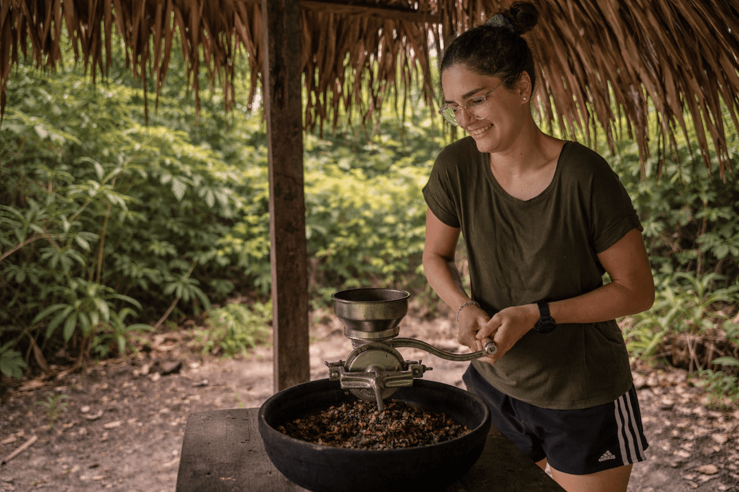 Huésped sonriente moliendo cacao a mano durante una experiencia tradicional en la selva amazónica en Tucan Lodge, Ecuador